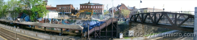 050511NatickRRStaPan PART 1 - Downtown Natick, Commuter Rail and Bicycle Parking.
The Natick Center Commuter Rail Station, with downtown Natick just beyond the Walnut Street pedestrian bridge and with the start of the CRT at extreme right. The 2001 mural celebrates Natick's 350th anniversary with various scenes from its past.
This panorama view is spliced from three photographs. To maximize (Zoom) it, tap your keyboard's 
