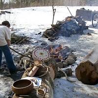 070303SyrupingIndianStyle In another exhibit, Mashpee Wampanoag Indians demonstrate how their inland neighbors maple sugared before the white man arrived. Behind a log exhibit of Native American craftmanship, a young lady heats rocks in an open fire. (No, she's not burning the drum.) The log trough was hollowed by placing glowing coals into the log on the right, charring and hacking it into a holder for a lot of maple sap. Then it was scraped clean. Now, sap is being boiled by putting in hot rocks from the fire. The log would burn in the fire, but even birch-bark bowls can boil water by transferring the hot rocks into their liquid contents. Good idea!
